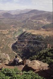 Image du Maroc Professionnelle de  Un berbère accompagné de sa chèvre assis sur des rochers qui surplombent un paysage d'une des vallées du Haut Atlas sur la route à travers  la montagne qui mène de Marrakech à Ouarzazate le Dimanche 24 Août 1997. (Photo / Abdeljalil Bounhar)
